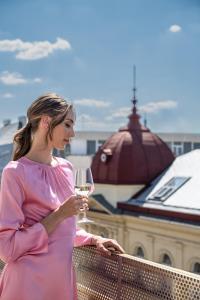 une femme debout sur un balcon tenant un verre de vin dans l'établissement Almanac X Alcron Prague, à Prague