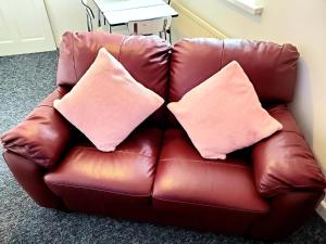 Un sofá de cuero marrón con dos almohadas rosas. en The Quiet Room, en Newcastle