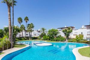 a swimming pool with palm trees and buildings at Escape to Serenity - 3 Bedroom Townhouse by the Sea! in Marbella