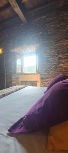 Cama con almohadas moradas en una habitación con ventana en Apartamentos Rurales El Bosque de las Viñas, en Boal