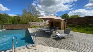 una terraza con sillas y una sombrilla junto a la piscina en Domaine de l'Epau Eco-Resort - Eco-Lodges, en Yvré-lʼÉvêque