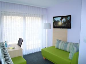 a living room with a green couch and a tv on a wall at Hotel Brehm in Würzburg