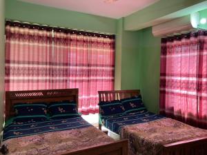two beds in a room with red curtains at Hotel Surma Residential in Dhaka