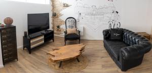 a living room with a black leather couch and a tv at UNE PARENTHESE ARDENNAISE in Charleville-Mézières