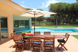 einem Holztisch mit Stühlen und einem Sonnenschirm neben einem Pool in der Unterkunft Villa Jackson in Vilamoura