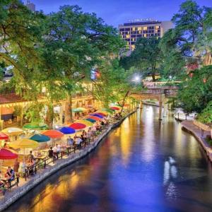 a river with tables and umbrellas next to a city at The Alamo Riverwalk Pearl Modern 4 Bedroom Home in San Antonio