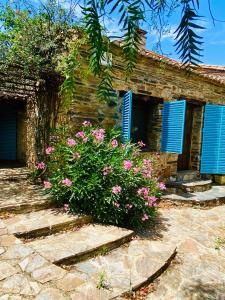 Casa de piedra con persianas azules y flores rosas en Casa La Rocita, en Badajoz