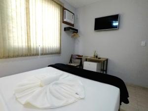 a bedroom with a white bed and a tv on the wall at Suítes do Cabo in Arraial do Cabo