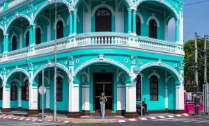 une femme debout devant un bâtiment bleu dans l'établissement The Tint At Phuket Town - SHA Plus, à Phuket