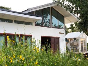 een huis met glazen ramen en een bloemenveld bij The Little Clay House (Huahin) in Ban Thap Tai (1)