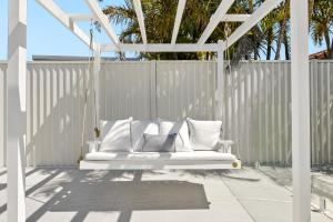 a white swing on a patio with a fence at Paradise Palms Mooloolaba - Beach House in Mooloolaba