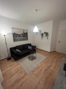 uma sala de estar com um sofá preto e um piso de madeira em Lichtung Appartement - *WLAN**Netflix**Stadion-Nah* em Leipzig