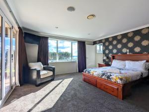 a bedroom with a bed and a chair and windows at Luxury Lake View farm stay with spa pool in Rotorua