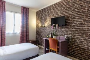 a hotel room with a brick wall and a desk with a tv at Hôtel HAPY in Houdan