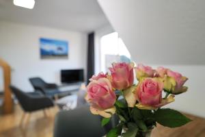 a vase filled with pink roses in a living room at HAUSTIERFREI - Ferienwohnung Meerfarbig Zingst - GLASFASER -Balkon - Parkplatz - Fahrradschuppen - zentral&ruhig - E-Ladesäule - Waschtrockner - Nichtraucher - allergikerfreundlich in Zingst