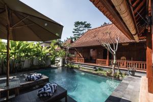 an outdoor swimming pool with an umbrella and a house at Meng Bengil Villa in Ubud