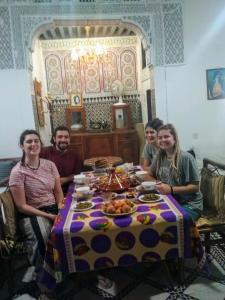 eine Gruppe von Menschen, die an einem Tisch mit Essen sitzen in der Unterkunft Fes Antique Hostel in Fès