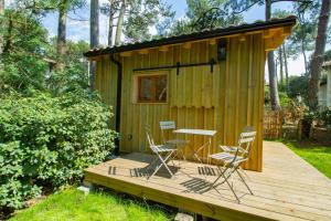 Cabaña de madera pequeña con sillas y mesa en una terraza en Cabane forêt proche plage en Pyla-sur-Mer