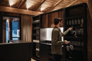 un homme debout devant une étagère avec un verre de vin dans l'établissement Luxury Spa Chalet Lum d'Or, à Selva di Val Gardena