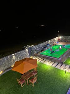 a table with an umbrella next to a pool at night at JA view chalet in Duwaykhīlah
