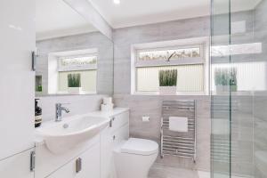 a white bathroom with a toilet and a sink at Luxury 5 BDR 2 BA House with Parking in Sandhurst By 360Stays in Sandhurst