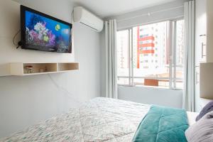 1 dormitorio con TV de pantalla plana en la pared en Amplo e iluminado apto central para temporada, en Balneário Camboriú