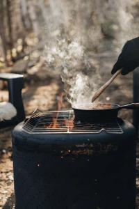 una persona che cucina cibo in padella su una griglia di Tanières MicroChalets Charlevoix a Baie-Saint-Paul