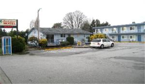 een witte auto geparkeerd op een parkeerplaats voor een gebouw bij Beach Grove Motel in Tsawwassen