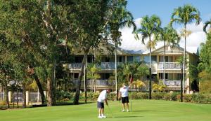 two men playing golf in front of a resort at Club Wyndham Cairns in Cairns