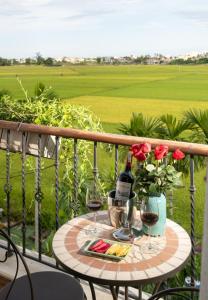 a table with two glasses of wine and flowers on a balcony at Maison Fleur Luxury Hoi An in Hoi An