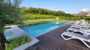 a swimming pool with white chairs and an umbrella at Villa Clementina - Prosecco Country Hotel in San Pietro di Feletto