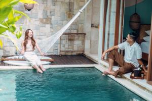 a man and a woman sitting in a hammock in a pool at Aksari Villa Seminyak by Ini Vie Hospitality in Seminyak