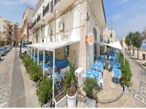 ジョヴィナッツォにあるIL Marinarettoの青いテーブルと白い傘が並ぶ通りのレストラン
