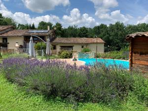 uma casa com um quintal com flores roxas e uma piscina em Gîte Bois et Senteurs em Lafrançaise