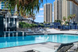uma piscina com cadeiras, palmeiras e edifícios em No Parking - Converted Two Bedroom Apartment - Amazing Hinterland Views - Circle on Cavill - Wow Stay em Gold Coast