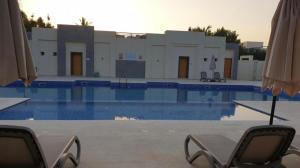 una piscina con 2 sillas y una sombrilla en Hawana Salalah Marina Studio ستوديو في مارينا هوانا صلاله en Salalah