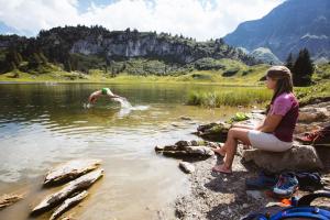 a woman sitting on the edge of a lake watching a man swimming at Hus23 in Schröcken