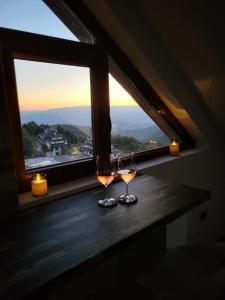 two glasses of wine sitting on a table in front of a window at Kloudscape Apartman Milmari Resort & Spa in Kopaonik