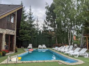 a swimming pool with white chairs and a house at Vila Zlatibor in Zlatibor