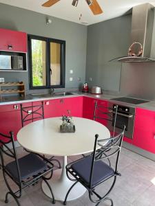 cocina con mesa blanca, sillas y armarios rojos en Maison avec terrasse proche Grignan en Colonzelle