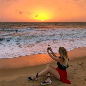 Bivon Reach By Travel Corners في أوسويتاكياوت: امرأة جالسة على الشاطئ تأخذ صورة لغروب الشمس