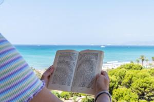 a person holding a book in front of the beach at Leman Hotel y Apartamentos in Playa de Palma