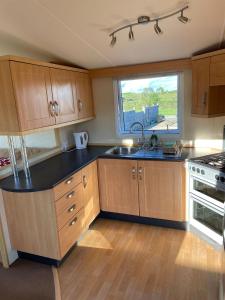 uma cozinha com armários de madeira, um lavatório e uma janela em Garej Mynytho Caravan em Pwllheli