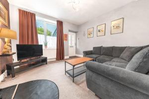 a living room with a gray couch and a television at Sunny Brae, Windermere Cottage in Windermere