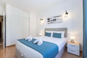 a white bedroom with a large bed with blue sheets and pillows at Beachside Bliss in Armação de Pêra