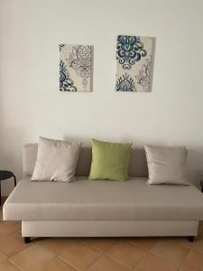 un sofá con 3 almohadas y 2 pinturas en la pared en La Chiocciola - Casa vacanze, en Erice