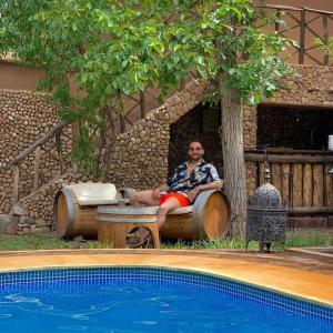 Riad Des Vieilles Charrues في بومالن: رجل جالس على كرسي بجانب مسبح