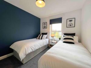 a bedroom with two beds and a blue wall at Beautiful Hatfield 2 Bedroom Apartment FREE Gated Parking - Modern Stylish - Business Park, Hertforshire University, St Albans, Welwyn Garden City, Luton Airport, Harry Potter Studio Tour in Hatfield