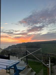 a view of a sunset from a deck with a bench at Sea View Nook in Porthtowan