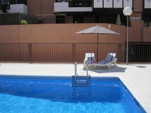 una piscina azul con sombrilla y 2 sillas en Apartamento Las Rozas Village, en Las Rozas de Madrid